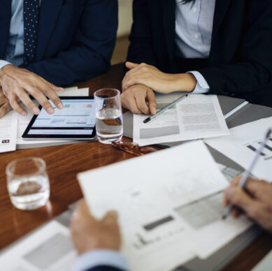 Businessmen and woman at boardroom table using digital tablet and working on paperwork, cropped